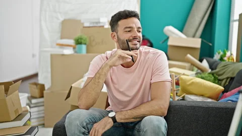 Young hispanic man sitting on sofa thinking at new home Video stock 245039362