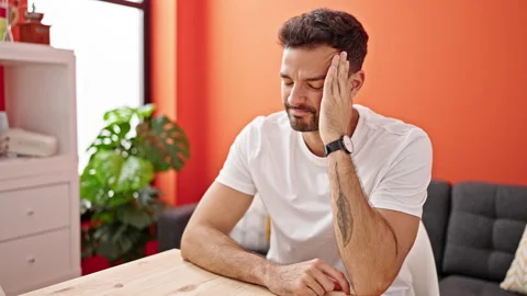 Young hispanic man sitting on table suffering headache at dinning room Stock Footage 245039253
