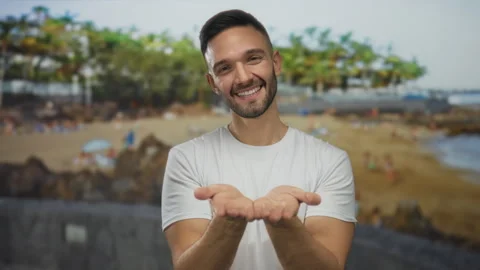 Young hispanic man smiling at the beach with hands extended towards the cam.. Stock Footage 313084764