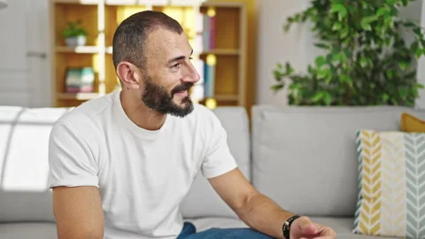 Young hispanic man smiling confident sitting on sofa speaking at home Stock Footage 245021113