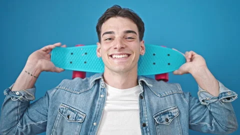 Young hispanic man smiling confident holding skateboard over isolated blue .. Video stock 246123225