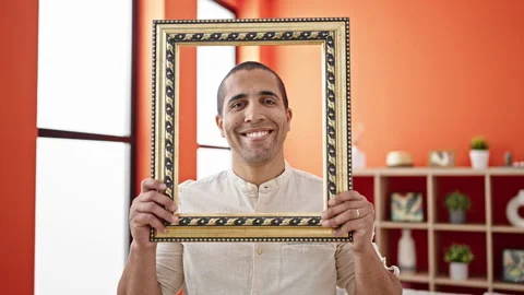 Young hispanic man smiling confident holding empty frame at home Stock Footage 246124868