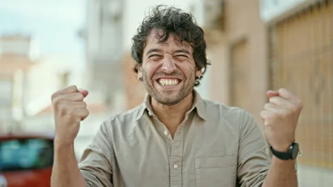 Young hispanic man smiling confident standing with winner gesture at street Stock Footage 247379266