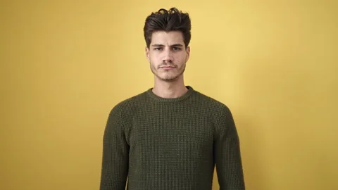 Young hispanic man standing with serious expression over isolated yellow ba.. Video stock 233416504