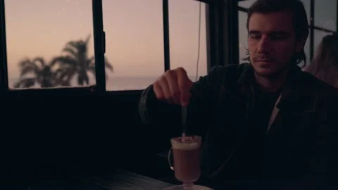 Young hispanic man stirs and drinks his coffee at sunset in a bar Stock Footage 201202601