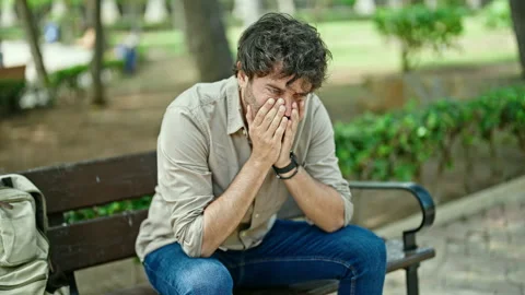 Young hispanic man stressed sitting on bench at park Video stock 246132586