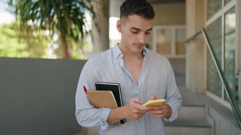 Young hispanic man student using smartphone holding books at street Stock Footage 206471834