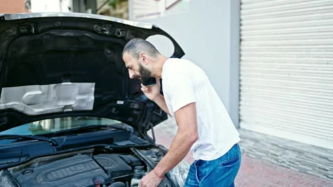 Young hispanic man talking on smartphone with insurance looking motor car a.. Video stock 245019951