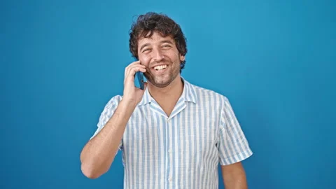 Young hispanic man talking on smartphone smiling over isolated blue backgroun Video stock 245559481