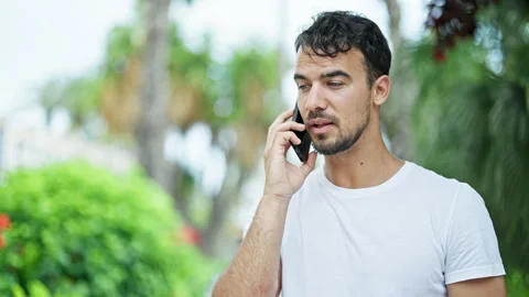 Young hispanic man talking on smartphone with serious expression at park Stock Footage 246126899