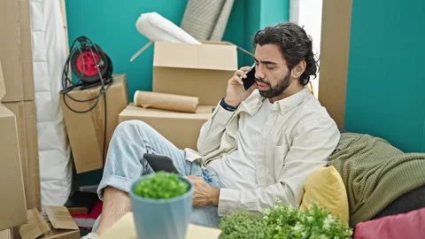 Young hispanic man talking on smartphone using touchpad at new home Stock-Footage 247378414