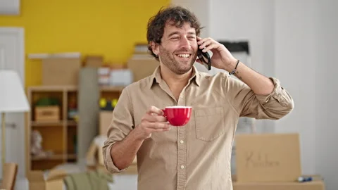 Young hispanic man talking on smartphone drinking coffee at new home Video stock 247379188