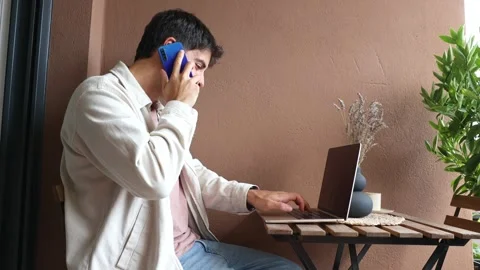 Young Hispanic man teleworking on laptop while talking on the phone Stock Footage 319027692