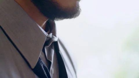 Young hispanic man tying a tie next to bright window Stock Footage 84482832