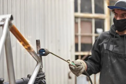 Young Hispanic man using a blowtorch to remove the paint of a bicycle frame Stock Photos