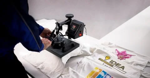 Young Hispanic Man Using Heat Press Machine To Print Custom Shirt Logo. Stock Photos