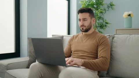 Young hispanic man using laptop sitting on sofa at home Stock Footage 180475298