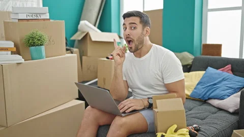 Young hispanic man using laptop sitting on sofa thinking at new home Video stock 243489958
