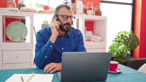 Young hispanic man using laptop talking on smartphone at dinning room Video stock 245020688