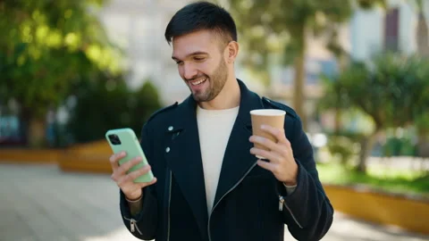 Young hispanic man using smartphone drinking coffee at park Video stock 170115489