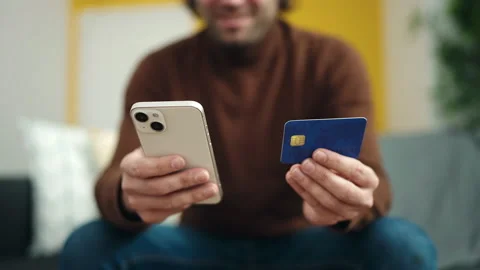 Young hispanic man using smartphone and credit card sitting on sofa at home Video stock 232873807