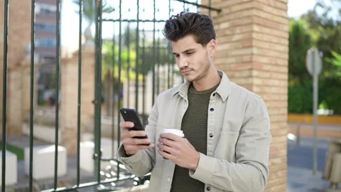 Young hispanic man using smartphone drinking coffee at street Video stock 233415849