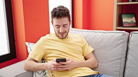 Young hispanic man using smartphone sitting on sofa at home Stock Footage 245044613