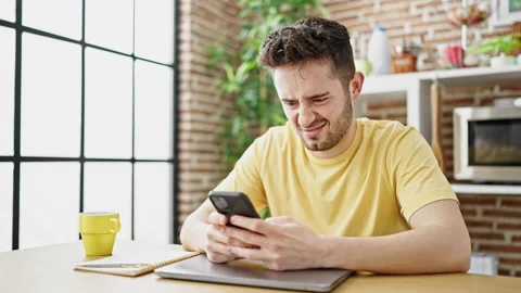 Young hispanic man using smartphone sitting on table at dinning room Stock Footage 245044829