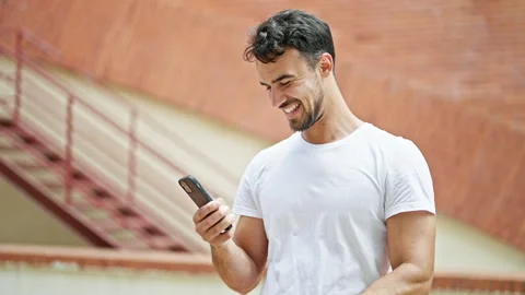 Young hispanic man using smartphone with winner gesture at street Video stock 246126822