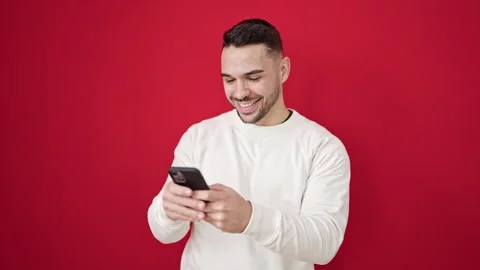 Young hispanic man using smartphone smiling over isolated red background Stock Footage 246134291