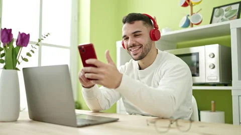 Young hispanic man using smartphone and headphones sitting on table at dinn.. Video stock 246134861