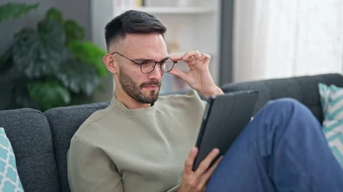 Young hispanic man using touchpad sitting on sofa at home Stock Footage 247382450
