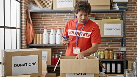 Young hispanic man volunteer using smartphone checking products at charity .. Video stock 246131990