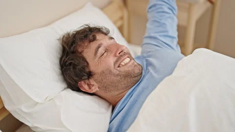 Young hispanic man waking up stretching arms at bedroom Stock Footage 245559065