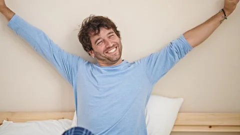 Young hispanic man waking up stretching arms at bedroom Video stock 246132328