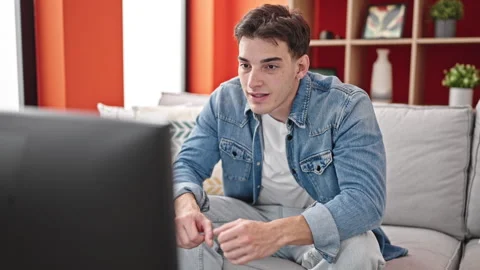 Young hispanic man watching tv sitting on sofa with winner expression at home Stock Footage 246123376