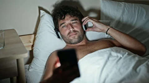 Young hispanic man watching video on smartphone lying on bed at bedroom Stock-Footage 247379233