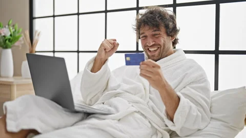 Young hispanic man wearing bathrobe shopping with laptop and credit card ce.. Video stock 245045057
