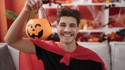 Young hispanic man wearing devil costume holding halloween pumpkin basket a.. Stockbeeldmateriaal 234652241