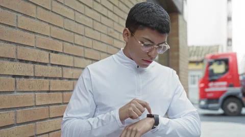 Young hispanic man wearing glasses and white pullover tapping smartwatch wi.. Stock Footage 337431404