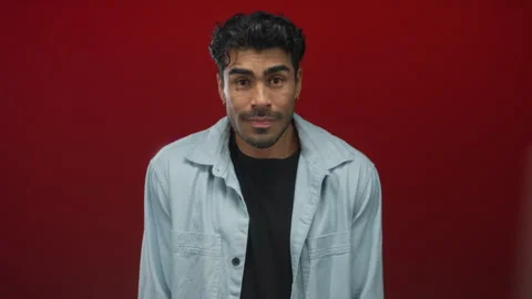 Young hispanic man wearing a light denim shirt smiles warmly in studio with.. Stock Footage 314629422