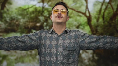 Young hispanic man wearing patterned shirt and sunglasses standing with arm.. Stock Footage 310980286