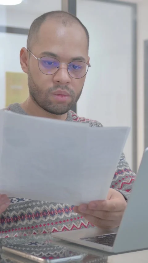 Young Hispanic Man Working on Documents and Laptop, vertical video Stock Footage 325567393