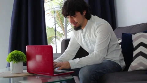 Young Hispanic man working happily from home with a computer in his living room Stock-Footage 142843672