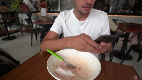 Young hispanic man writes a message on his phone after lunch Video stock 164452614