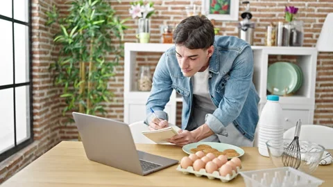 Young hispanic man writing on notebook online recipe at dinning room Stock-Footage 243481613
