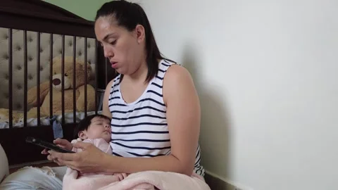 Young hispanic mom using her cell phone while taking care of her children Video stock 243176400