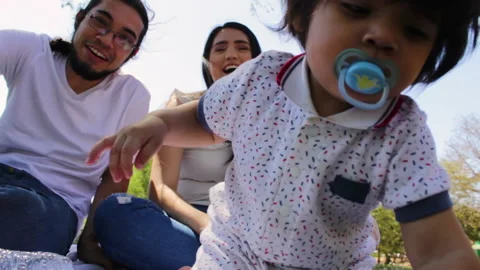 Young Hispanic parents playing with their one year old baby in a park Stock Footage
