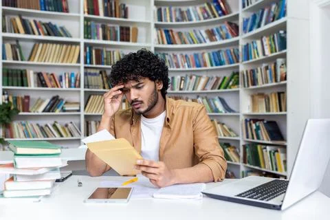 Young hispanic student upset studying inside university campus academic library 写真素材