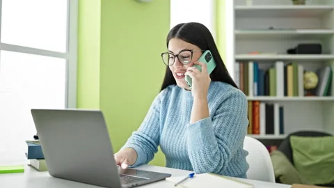 Young hispanic woman student using laptop speaking on the phone at library .. Stock-Footage 242364022